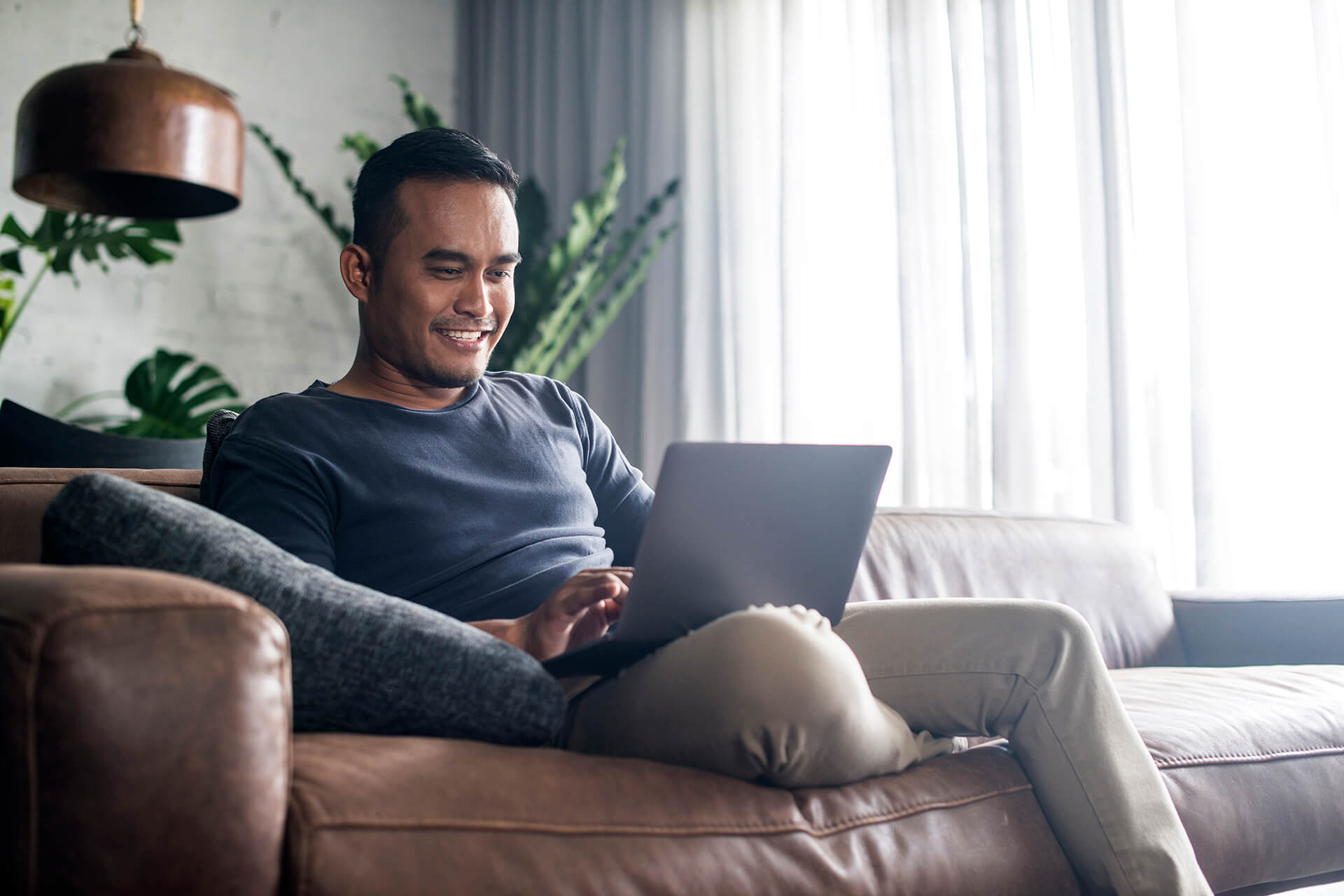 Young adult male relaxing on a couch using his laptop computer